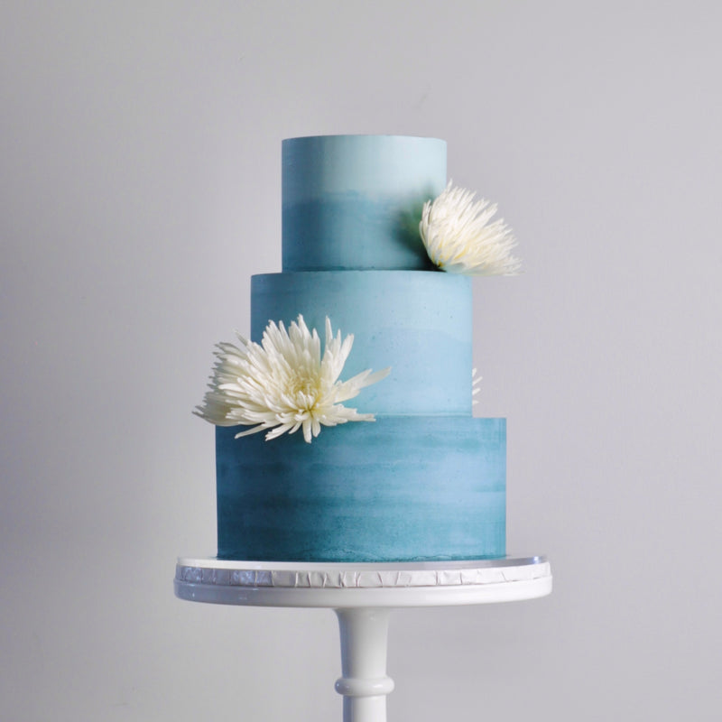 Three-tiered blue cake with white flowers on a gray background