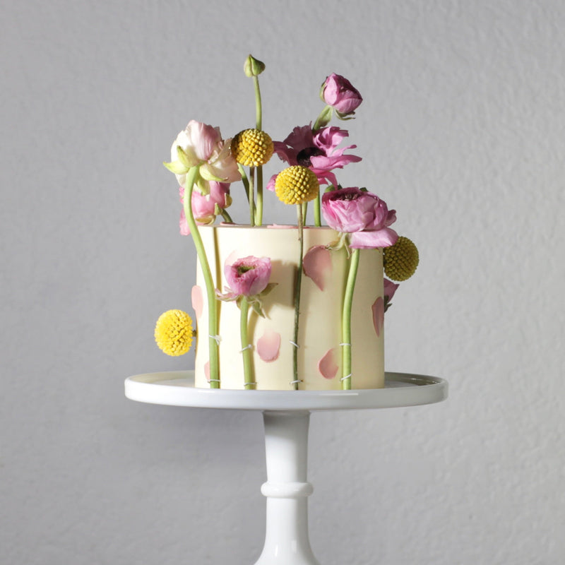 Decorative cake with flowers on a white stand against a gray background